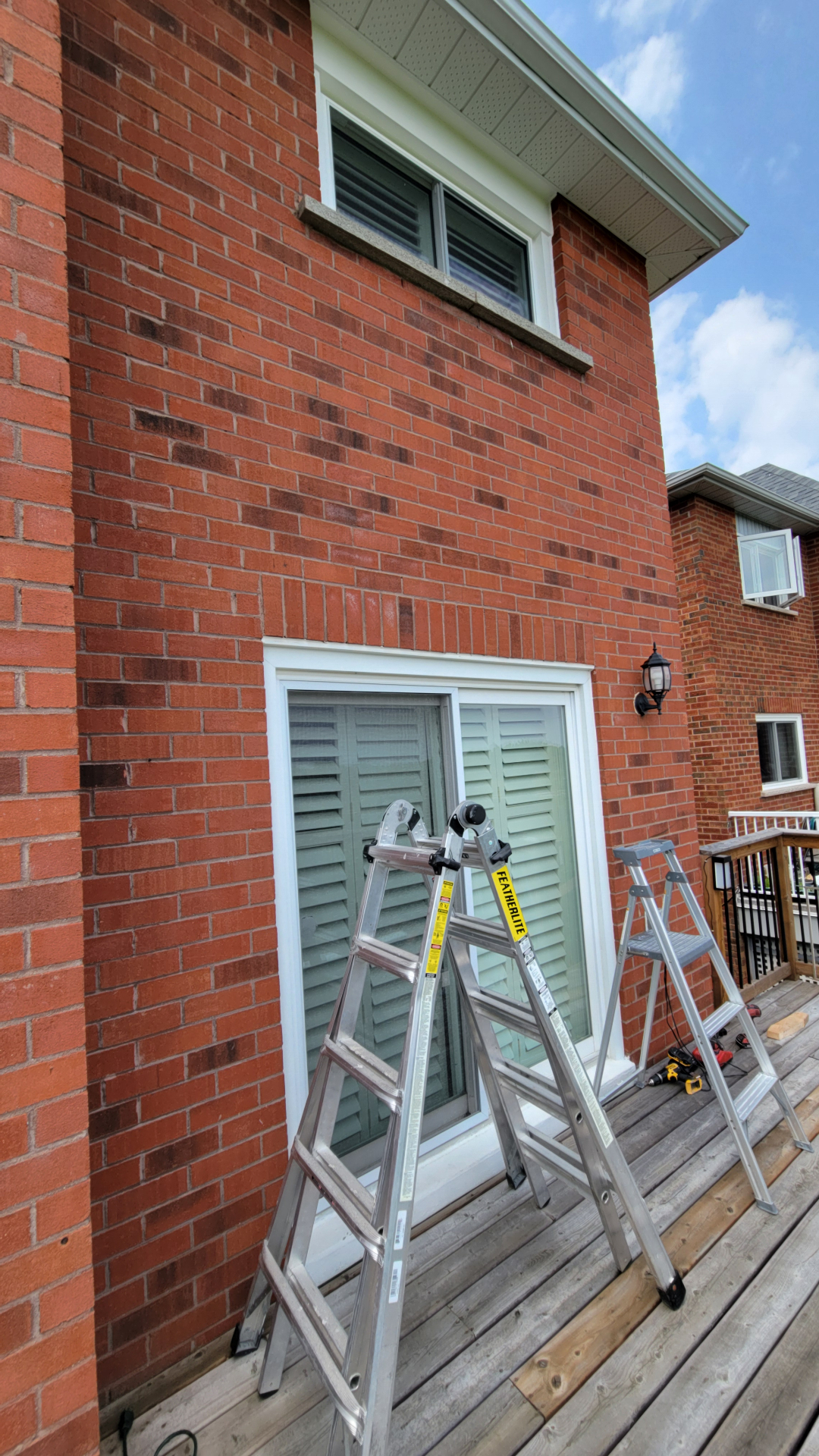 Newmarket back deck before awning install, ladders set up against brick wall above sliding patio door