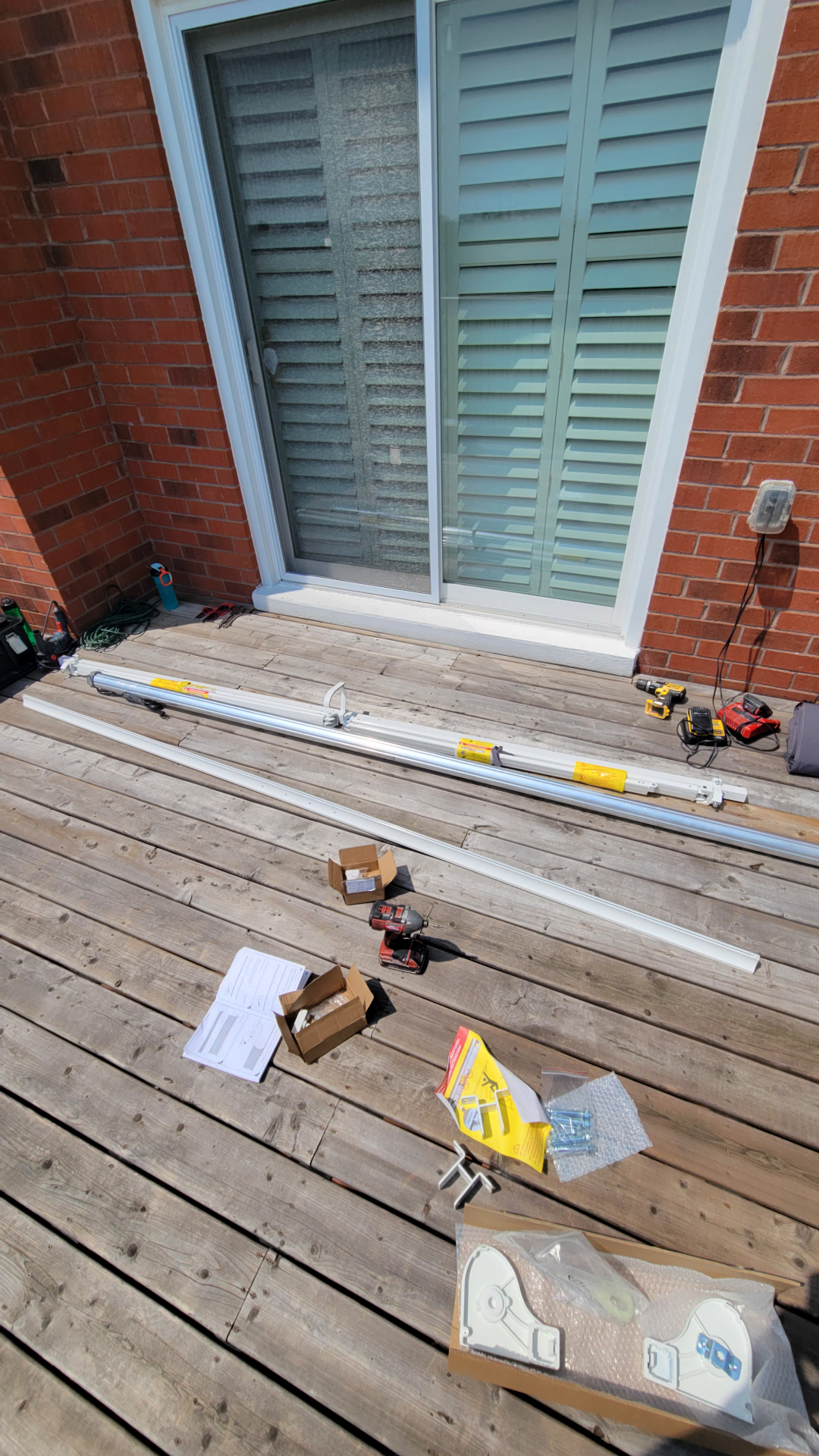 Retractable awning components, cassette, arms and hardware laid out on a cedar deck before installation