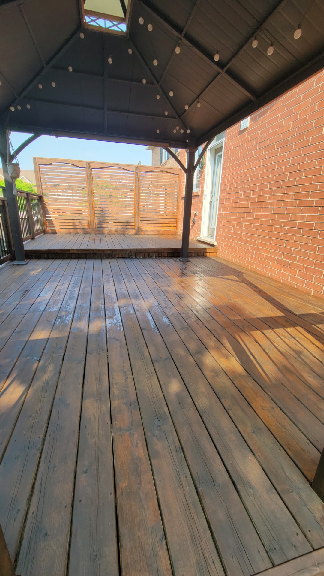 Close up of freshly stained cedar deck boards under a covered gazebo against a red brick wall
