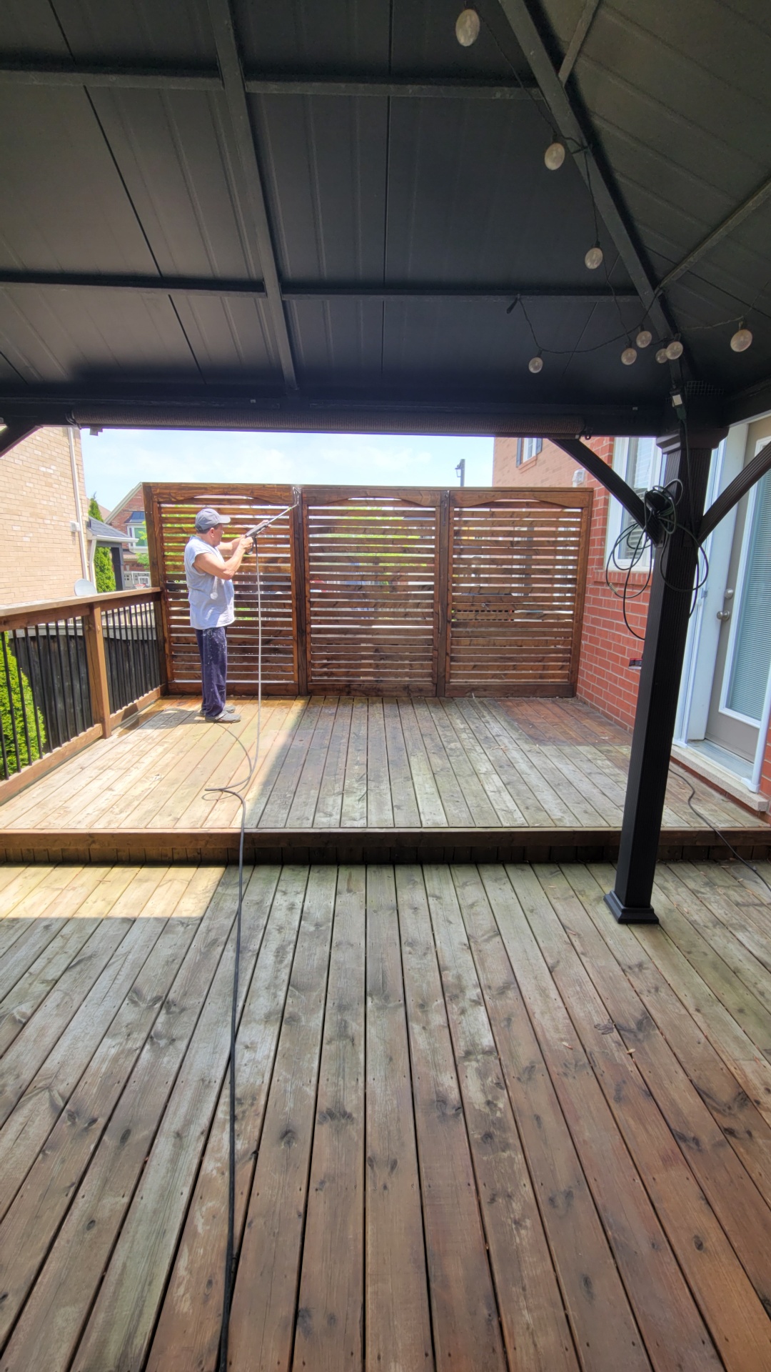 Power washing a wooden privacy screen on a Newmarket back deck under a covered gazebo