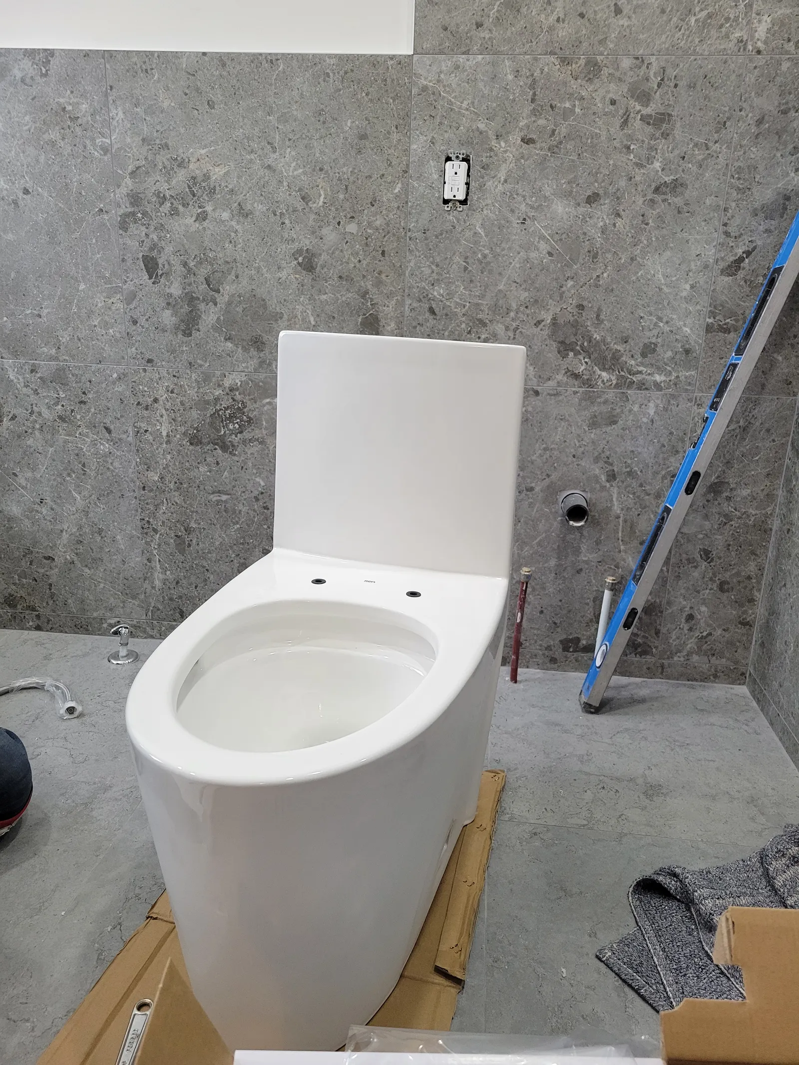New one-piece skirted toilet set against the grey-tiled wall in the Aurora bathroom