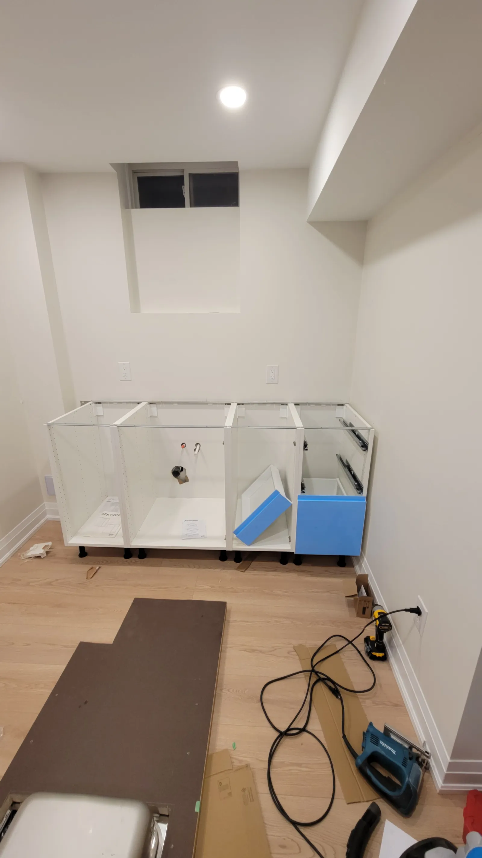 IKEA kitchen cabinet boxes being mounted to the wall in King City, with blue-fronted base cabinets below
