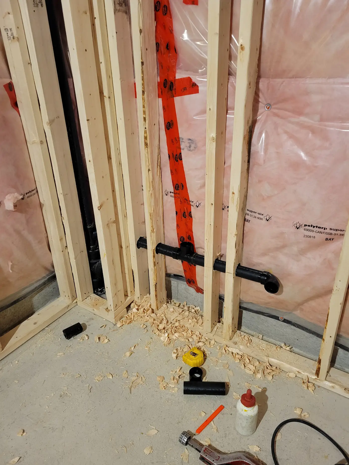 Black ABS drain and vent piping roughed in through wall studs for a laundry room in East Gwillimbury