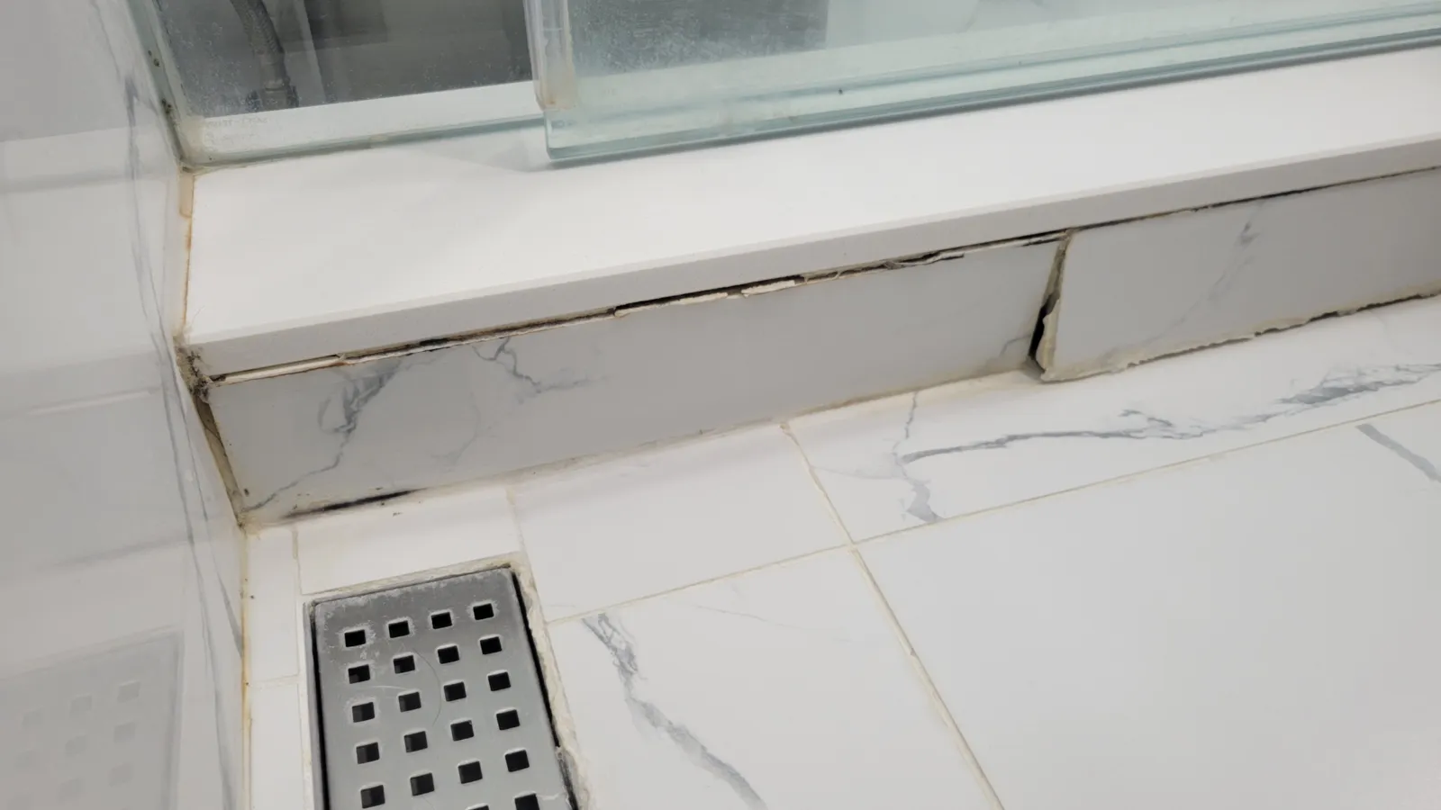 Failed shower curb in Newmarket with cracked grout, separating tiles and black mould along the joints