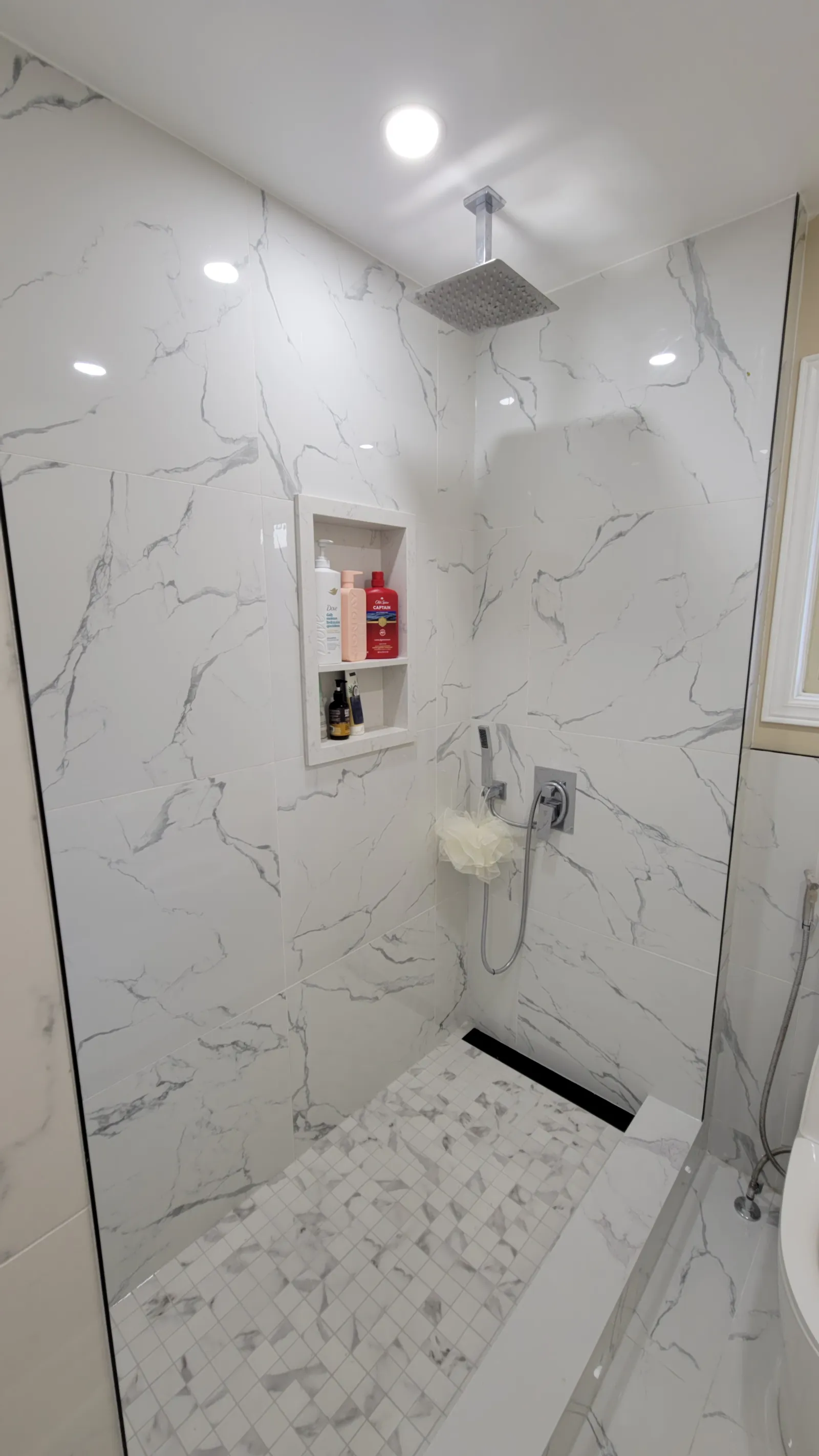 Finished rebuilt shower in Newmarket with marble-look porcelain, rain head, recessed niche and mosaic accent