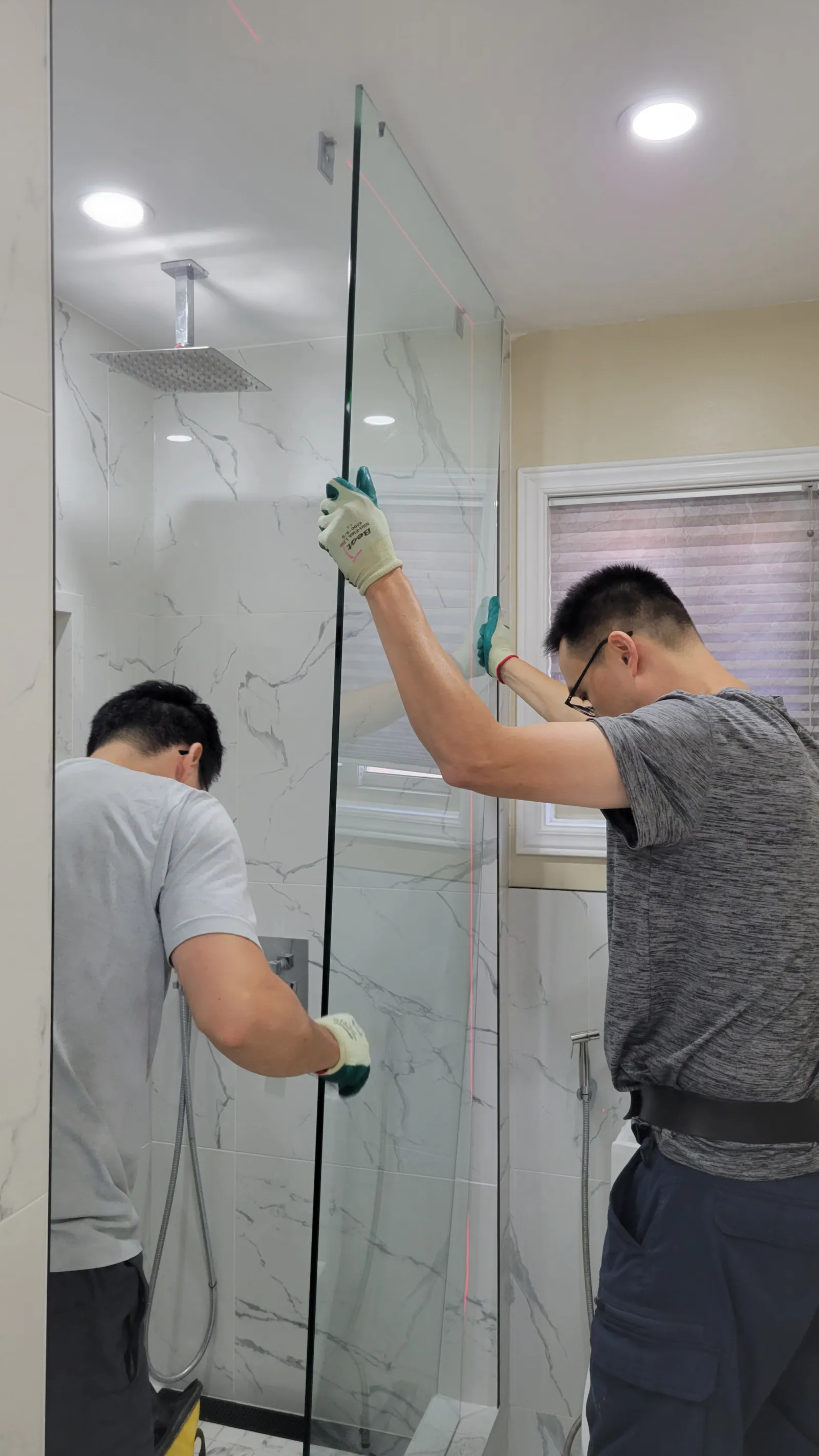 VOL Handyman installer setting the new frameless glass shower panel with a laser level in Newmarket