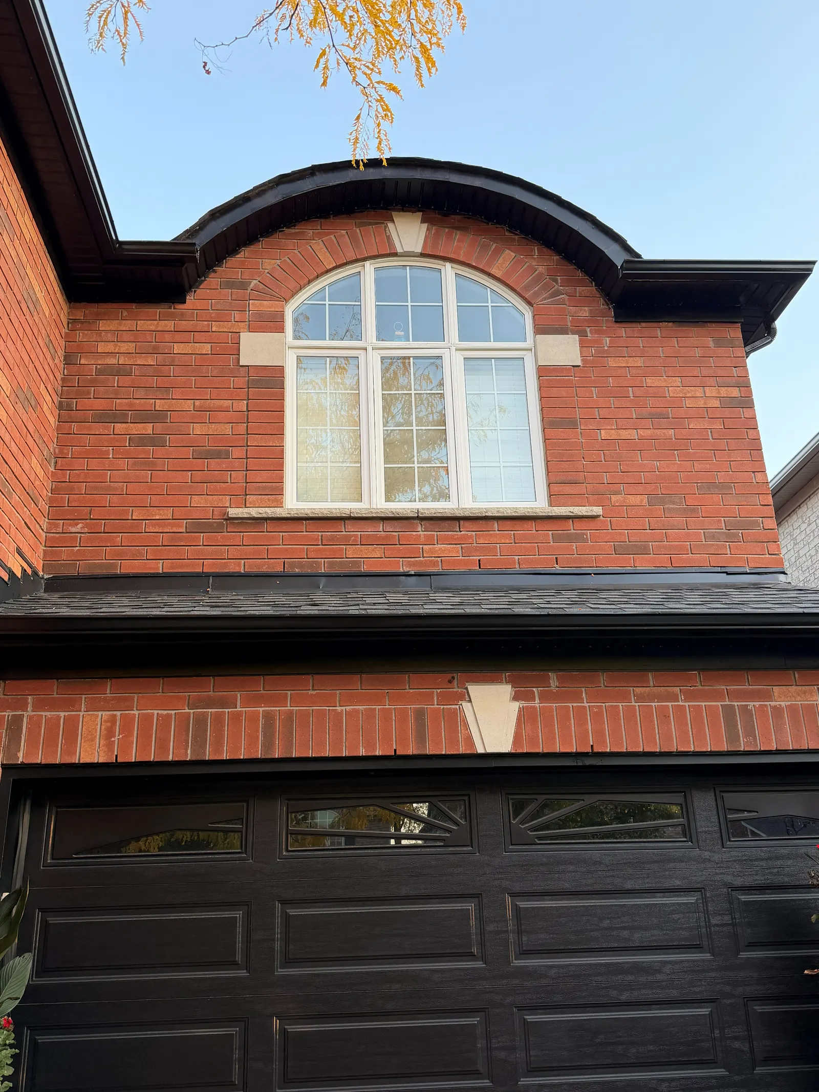 Curved dormer on a brick home with a freshly painted dark roofline, soffit and eavestrough above a white arched window