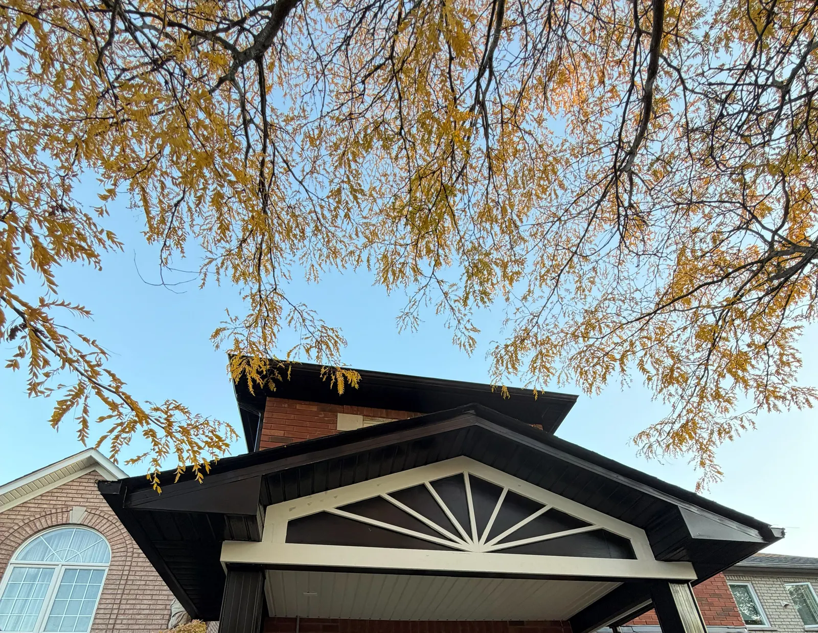 Front porch gable with dark soffit, fascia and downspouts and cream trim on a brick home in York Region