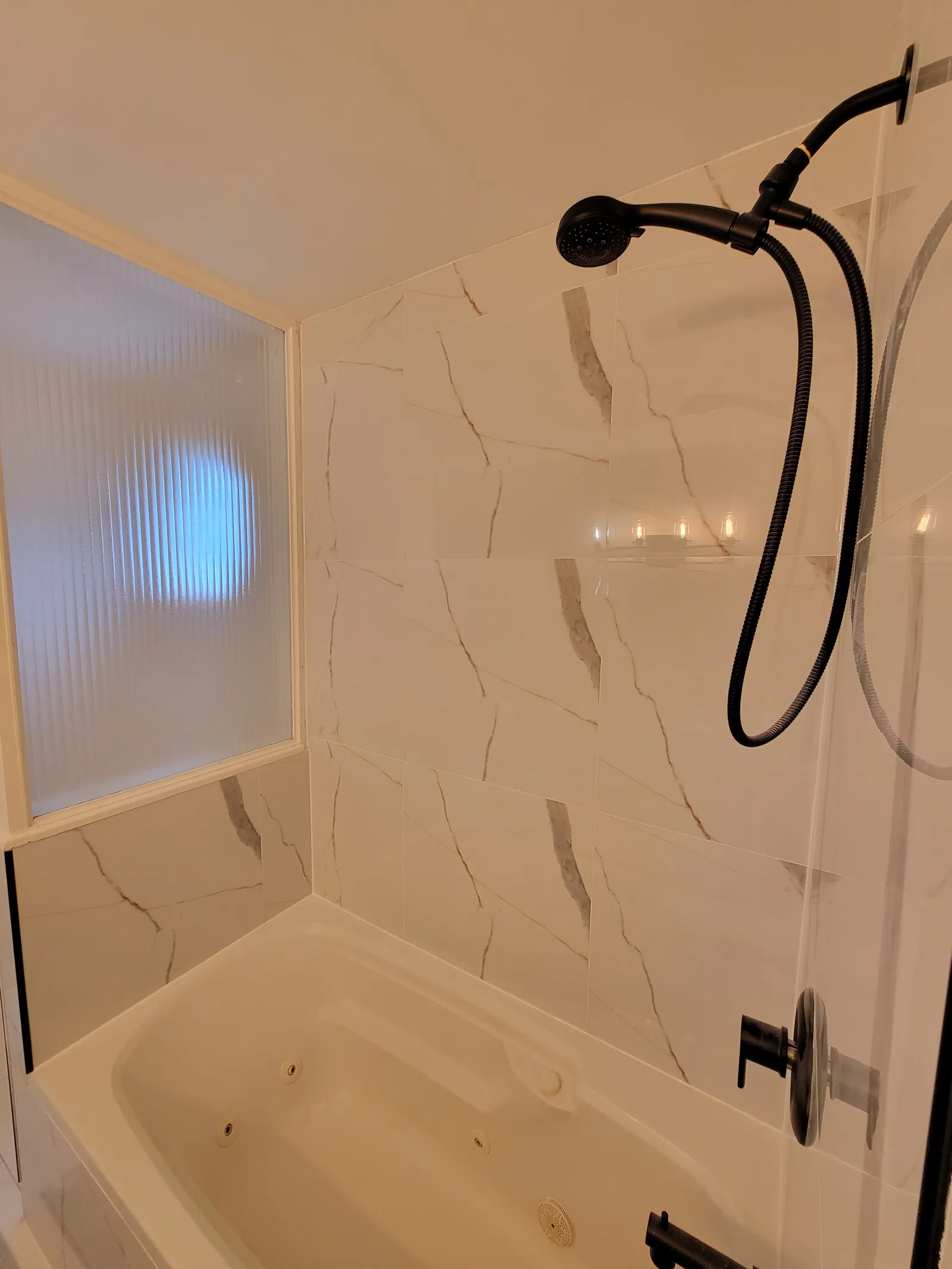 Lower-angle view of the finished Aurora tub surround with black hand shower, coiled hose and ribbed glass panel