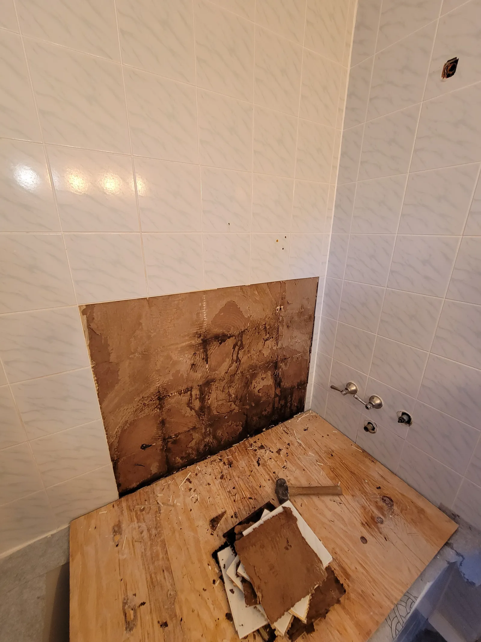 Old patterned white tile being removed from a bathtub surround in Aurora, exposing the mortar bed