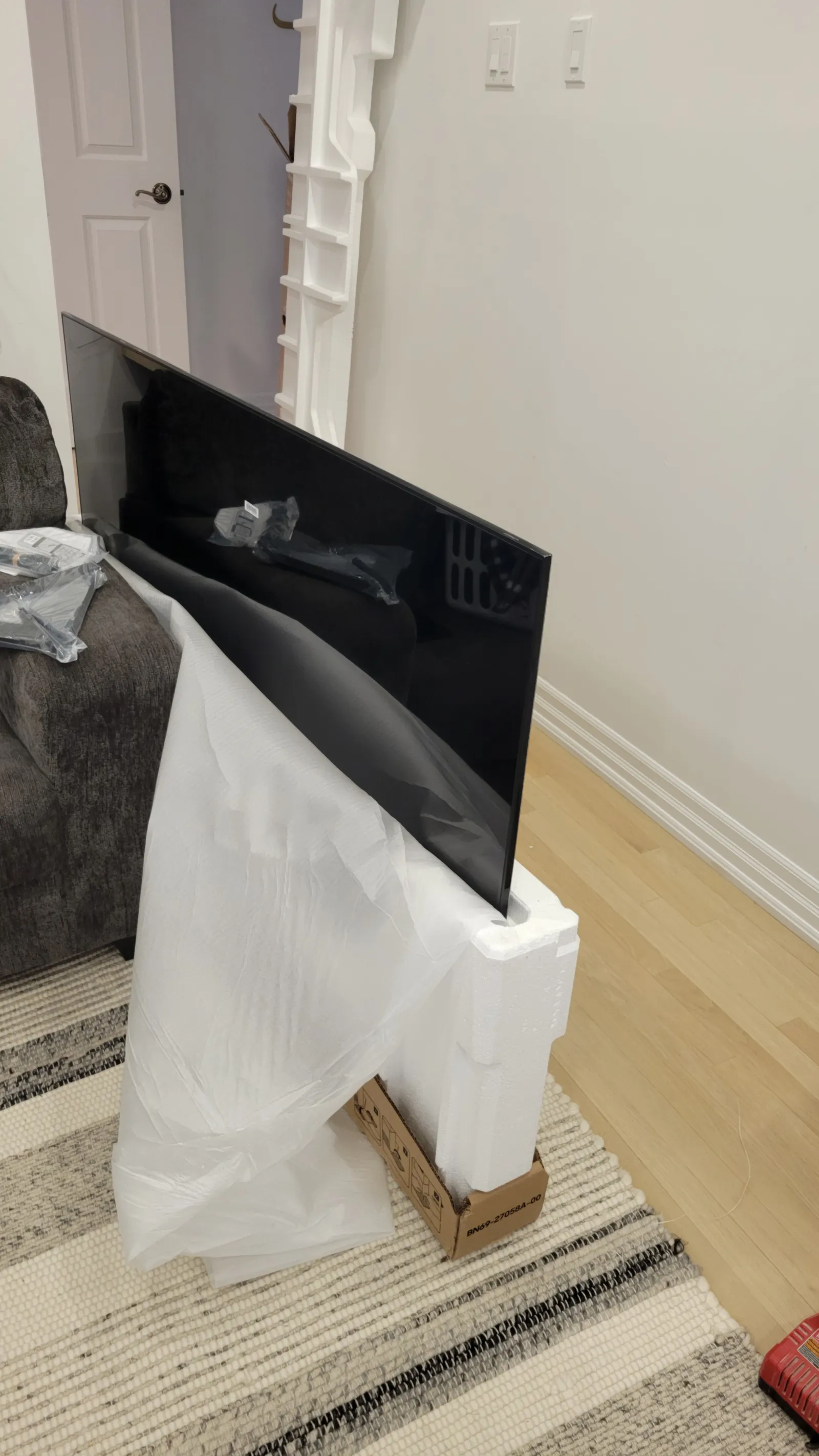 75-inch Samsung QLED unboxed and leaning against the sofa next to the full-motion mount hardware