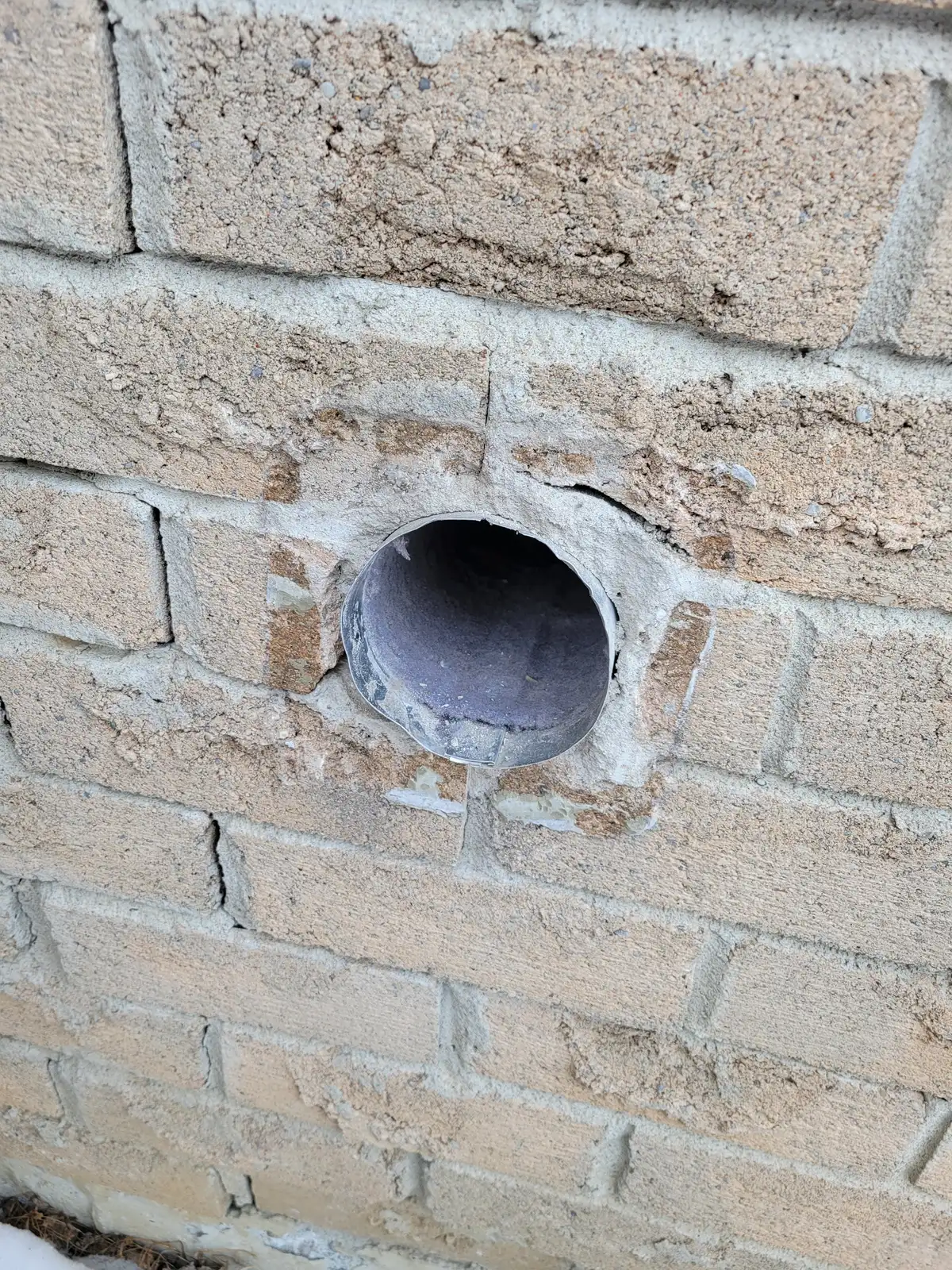 Bare metal dryer duct protruding through a brick exterior wall in Bradford with no vent cover
